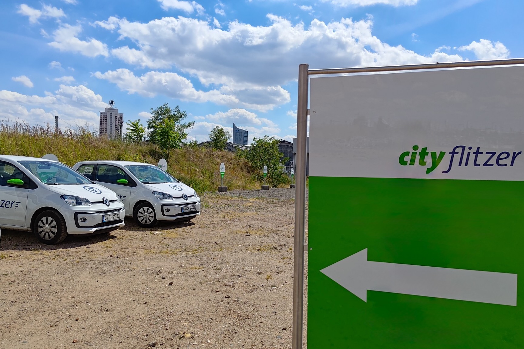 Der cityflitzer-Hub, im Vordergrund das Schild, im Hintergrund 3 Autos und der Leipziger Hauptbahnhof